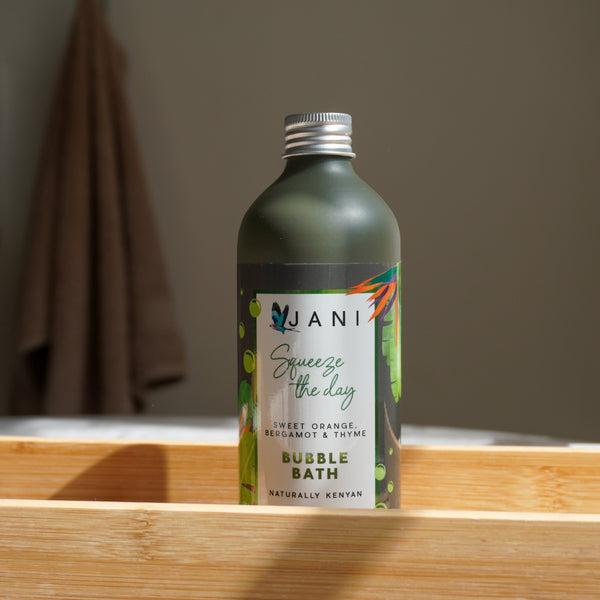 Bottle of JANI bubble bath on a wooden shelf with a blurred bathroom background