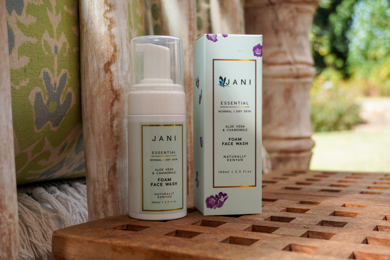 JANI essential foam face wash bottle and packaging on a wooden surface with a blurred natural background